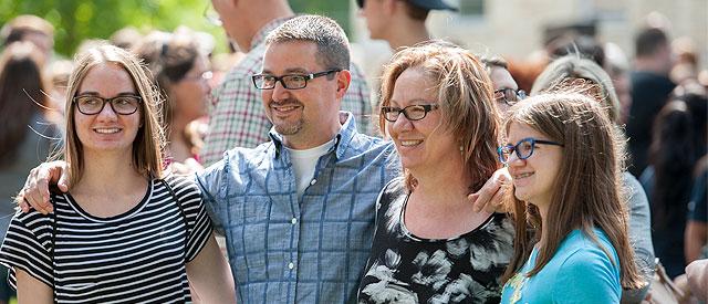 A group of four people, possibly a family, smiling and posing for a photo together in an outdoor setting crowded with people.